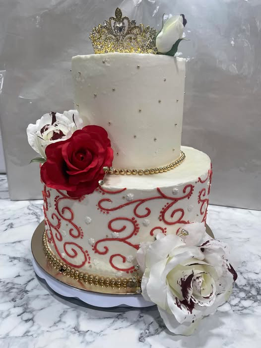Two-tier custom celebration cake with red scroll piping, roses and a gold crown